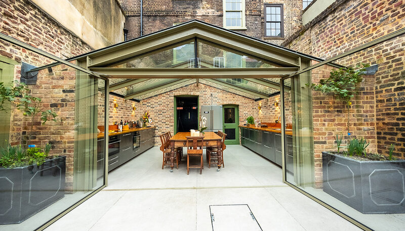 Frameless glass kitchen extension with slim aluminium frames and pitched glazed roof, inspired by red window frames.
