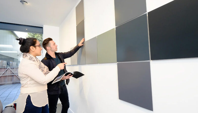 Two people reviewing architectural colour and glazing finish samples in the showroom, reflecting on the choice of red window frames.