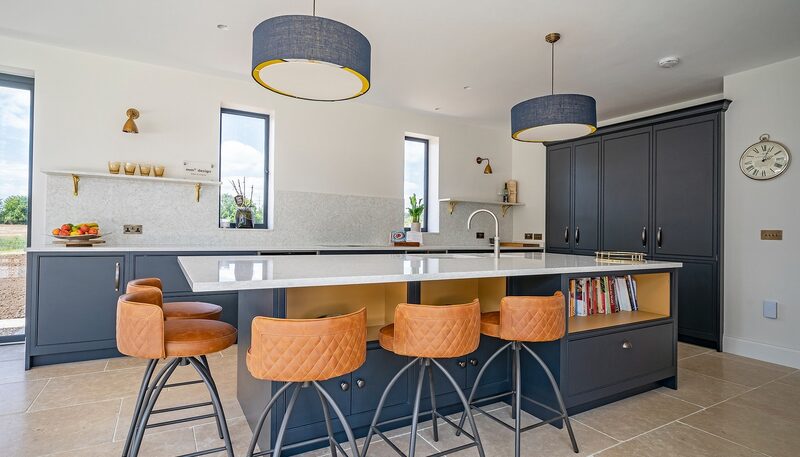 Porcelain vs quartz worktops: Dairy Farm kitchen by Watermark Kitchens with navy cabinetry, a pale island worktop and tan bar stools.