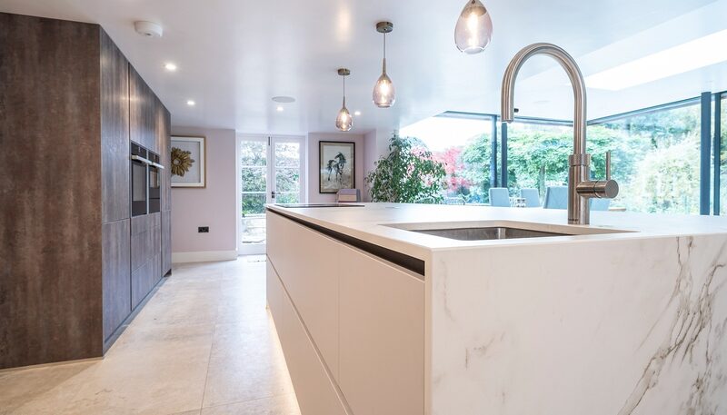 Porcelain vs quartz worktops: Watermark kitchen island with a pale veined waterfall end, sink and tall curved tap.