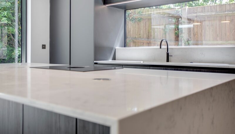 Porcelain vs quartz worktops: pale island worktop and black tap beneath a wide window in a Watermark kitchen.